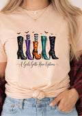 A woman wearing a light peach t-shirt with a graphic of five colorful witch boots and the text 'A Girl's Gotta Have Options', paired with blue jeans and a red plaid shirt.