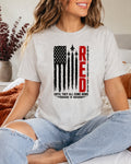 A woman wearing a light heather gray graphic t-shirt with a distressed American flag design and the word 'RED' in vertical red letters, paired with ripped light blue jeans.