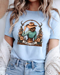 A woman wearing a light blue graphic t-shirt with a western-themed illustration of a woman in a hat and the text 'THE HELL I WON'T'.