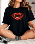 A woman sitting cross-legged on a bed wearing a black t-shirt with a graphic of red vampire lips with white fangs.