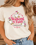 A woman wearing a cream-colored graphic t-shirt with a cartoon duck design and the text 'Walking by Faith Tripping Constantly'.