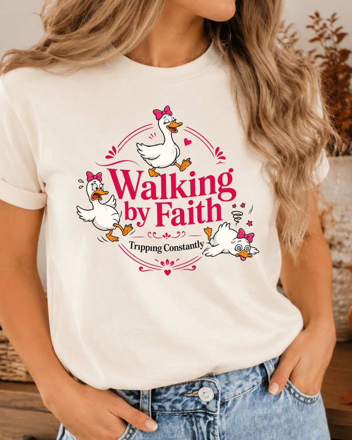 A woman wearing a cream-colored graphic t-shirt with a cartoon duck design and the text 'Walking by Faith Tripping Constantly'.