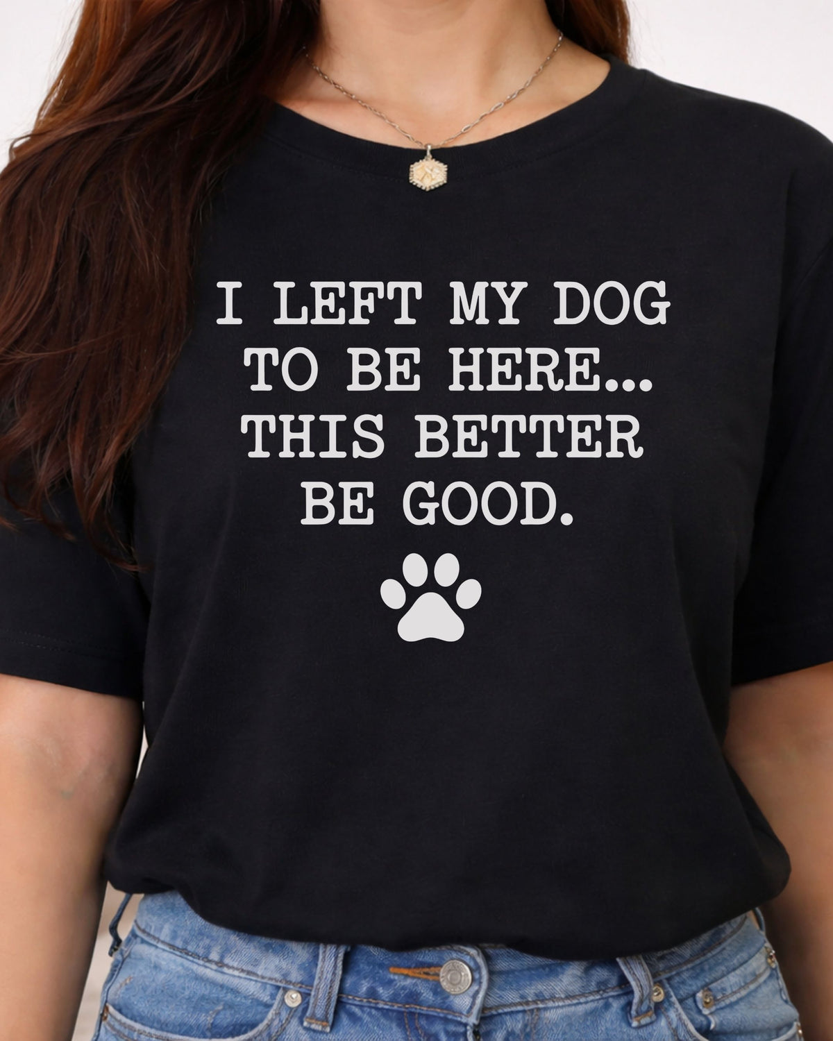 A woman wearing a black short-sleeve graphic T-shirt with the white printed text 'I LEFT MY DOG TO BE HERE.