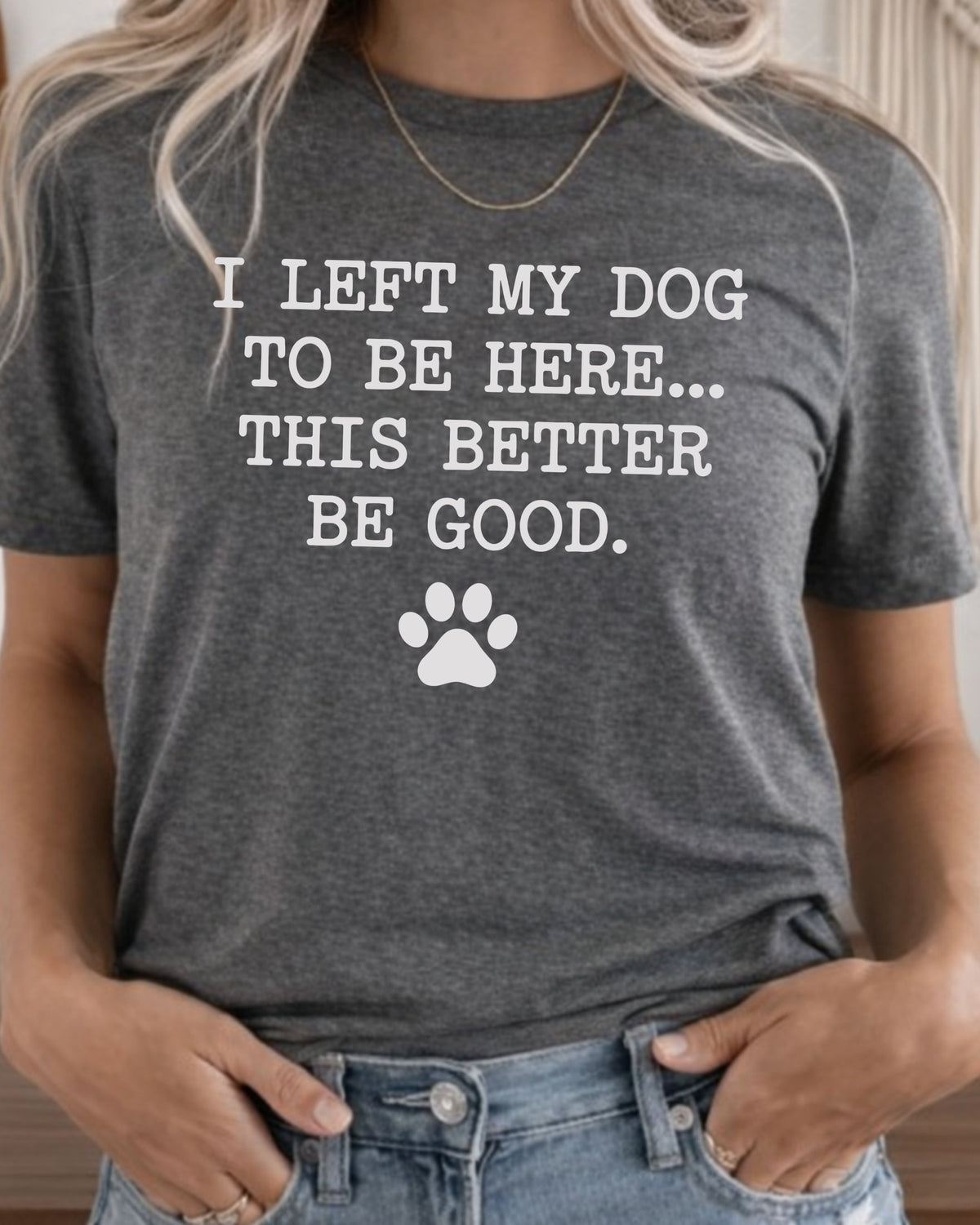 A woman wearing a dark heather gray graphic t-shirt with the white printed text 'I LEFT MY DOG TO BE HERE.