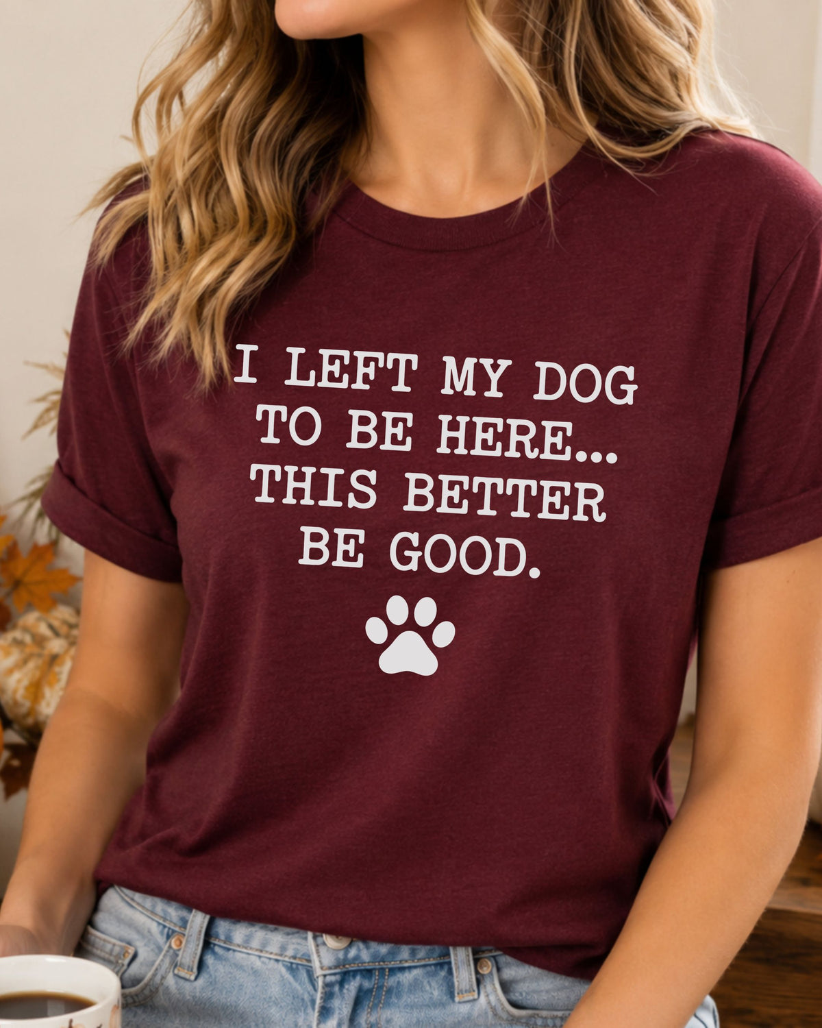 A woman wearing a maroon short-sleeve graphic t-shirt with the white printed text 'I LEFT MY DOG TO BE HERE.