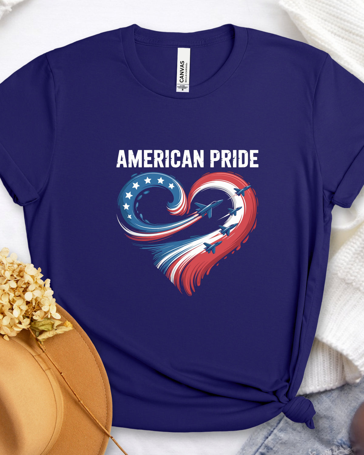 A navy blue short-sleeve t-shirt with a patriotic graphic on the front. The graphic features the text 'AMERICAN PRIDE' in white above a heart-shaped swirl design in red, white, and blue with stars and a small airplane.