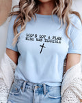 A woman wearing a light blue graphic t-shirt with the text 'GOD'S GOT A PLAN MINE WAS TERRIBLE' and a black cross printed on the front, styled with a white knit cardigan and denim shorts.