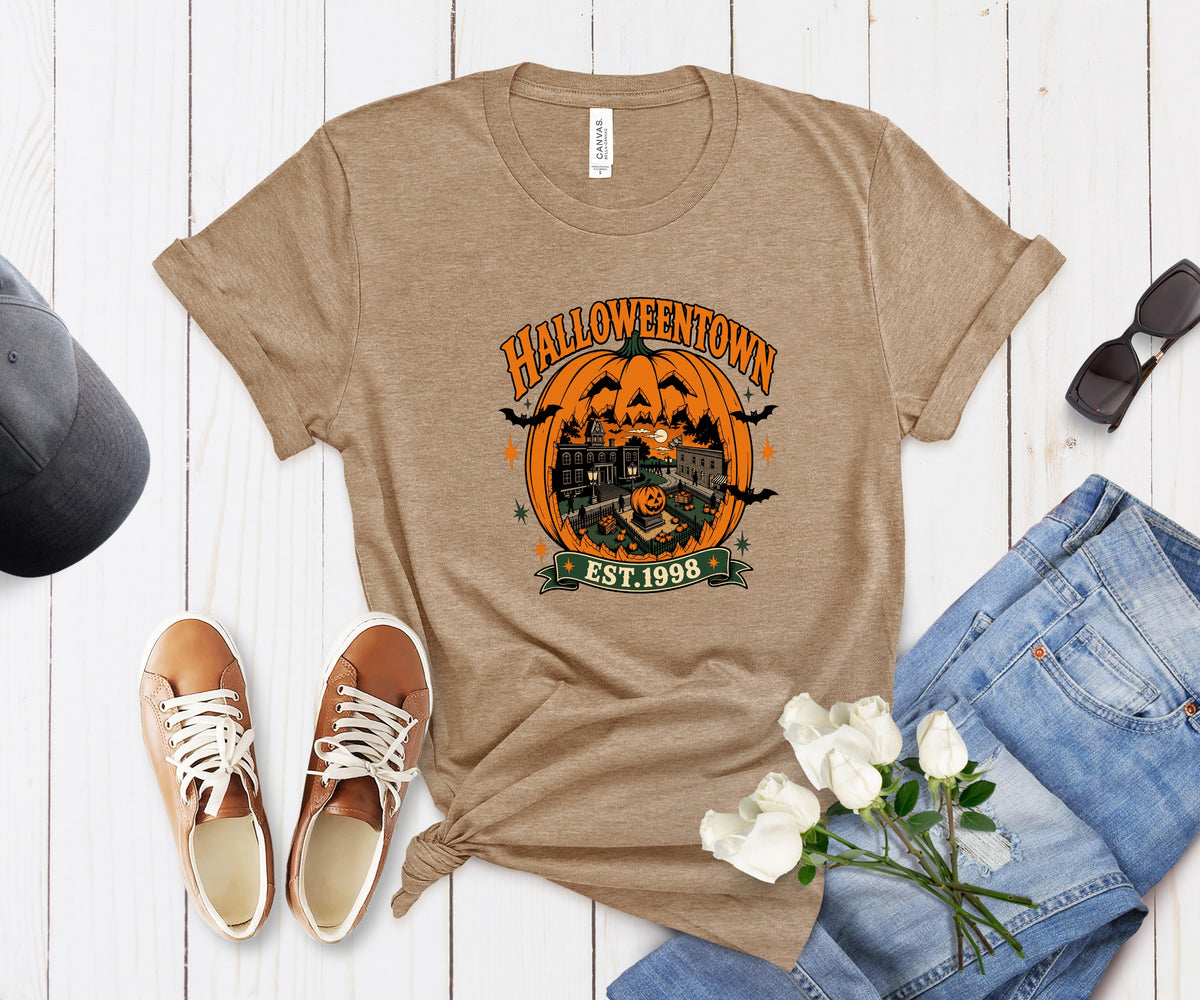 A tan graphic t-shirt with a Halloween-themed print reading 'HALLOWEENTOWN EST. 1990' and showing a jack-o'-lantern, haunted house, bats, and a witch.
