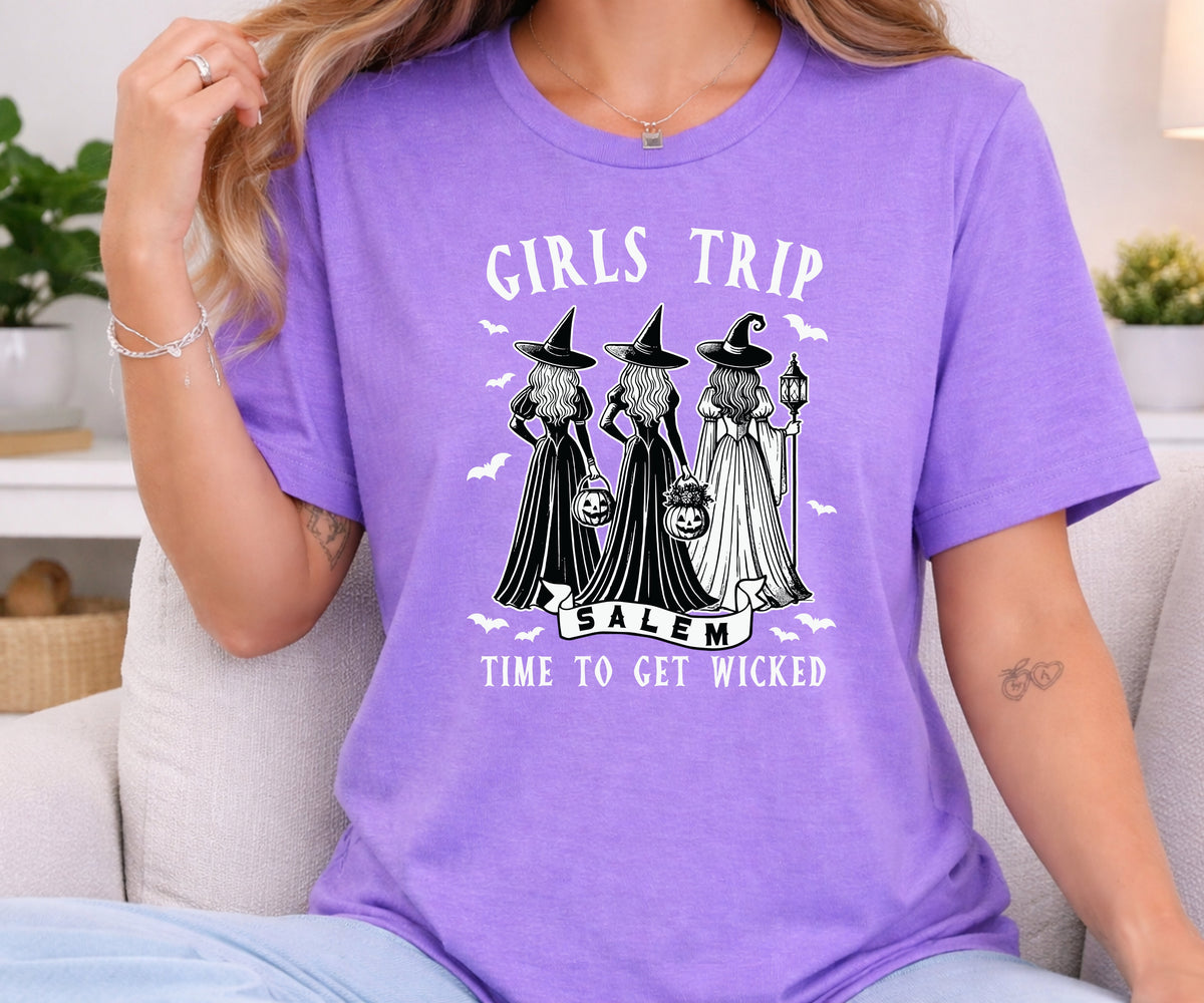 A woman wearing a purple graphic t-shirt with a black and white print of three witches in Salem, featuring the text 'GIRLS TRIP TO SALEM' and 'TIME TO GET WICKED'.