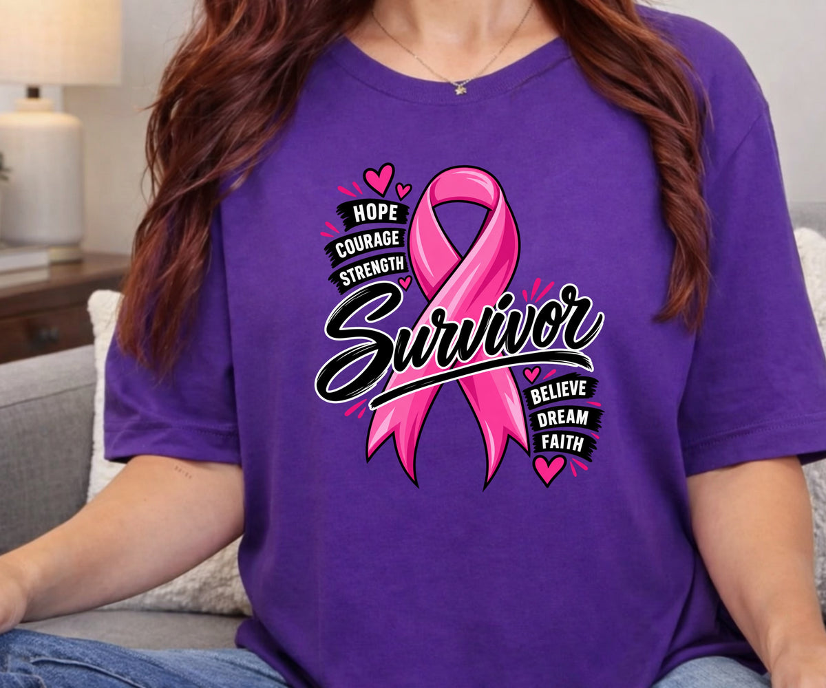 A woman wearing a purple short-sleeve graphic T-shirt with a pink ribbon and the words 'Hope Courage Strength Survivor Believe Dream Faith' on the front, seated on a couch in a living room setting.
