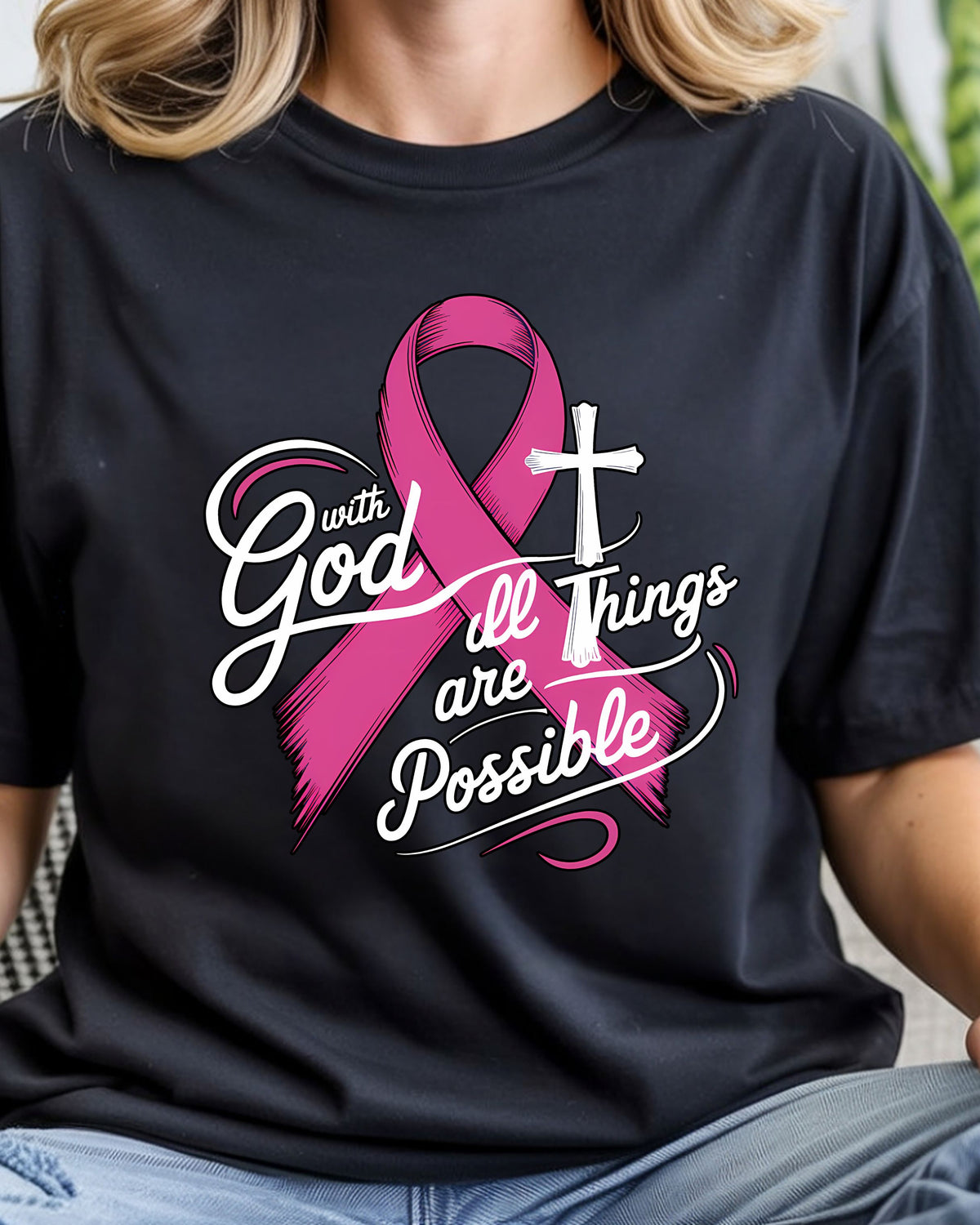 A person wearing a black short-sleeve T-shirt with a pink awareness ribbon, white cross, and the phrase 'with God all things are possible' printed on the front.