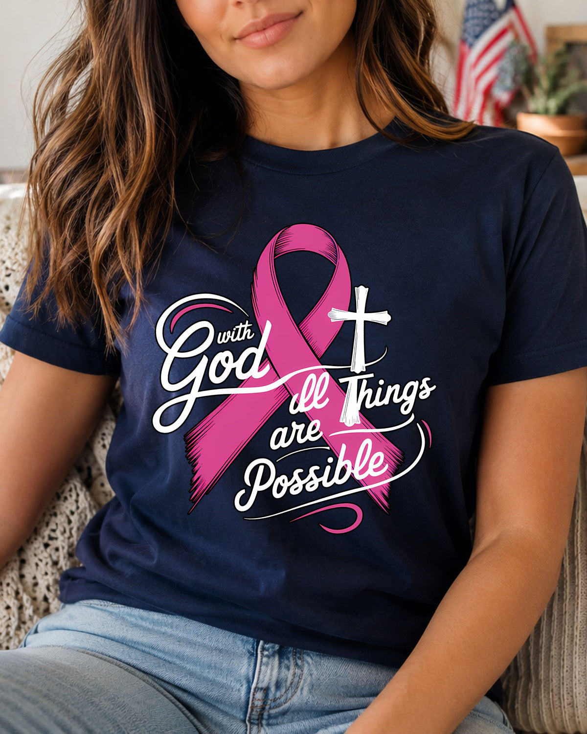 A woman wearing a navy blue graphic t-shirt with a pink breast cancer ribbon, a white cross, and the text 'with God all Things are Possible'.