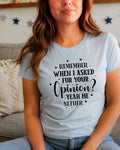 A woman wearing a light blue graphic t-shirt with black text that reads 'REMEMBER WHEN I ASKED FOR YOUR OPINION? YEAH HE NETHER' with small heart and dot accents, sitting on a couch in a living room setting.