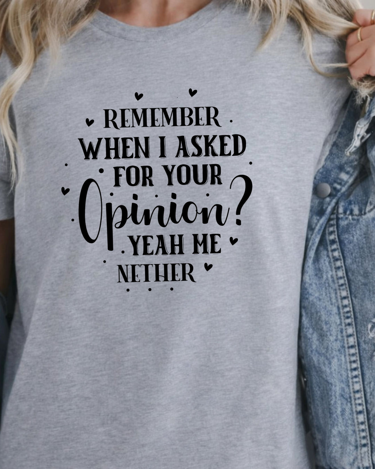 A close-up of a person wearing a heather gray graphic T-shirt with black text that reads, 'REMEMBER WHEN I ASKED FOR YOUR Opinion? YEAH ME NETHER,' styled with small heart and dot accents. A light blue denim jacket is partially visible on the right side.