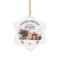 A white snowflake-shaped ceramic Christmas ornament hanging from a gold string. The ornament features a festive illustration of a small house, gift boxes, pine branches, and holiday decorations, with the text 'OUR FIRST CHRISTMAS in our HOME' and '2026' printed on it.