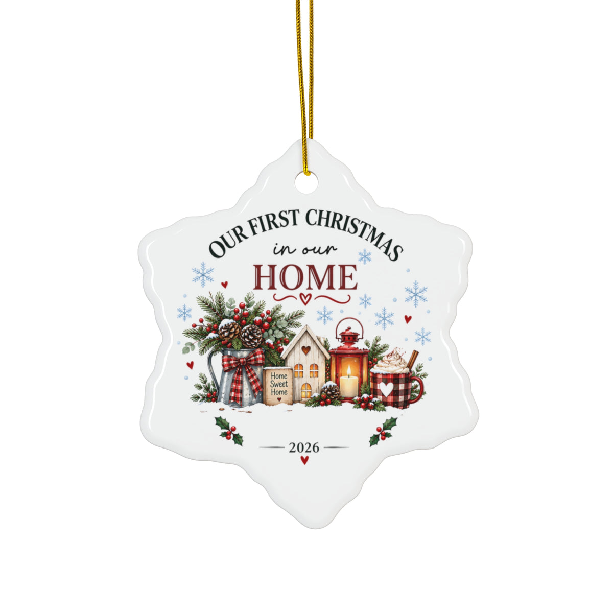 A white snowflake-shaped ceramic Christmas ornament hanging from a gold string. The ornament features a festive illustration of a small house, gift boxes, pine branches, and holiday decorations, with the text 'OUR FIRST CHRISTMAS in our HOME' and '2026' printed on it.